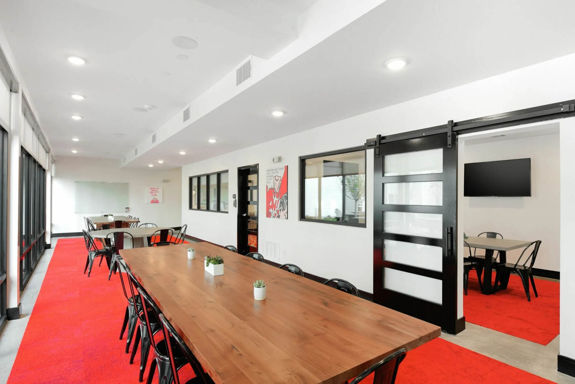 Conference or communal table in common space with rows of chairs modern lighting and a bright red rug